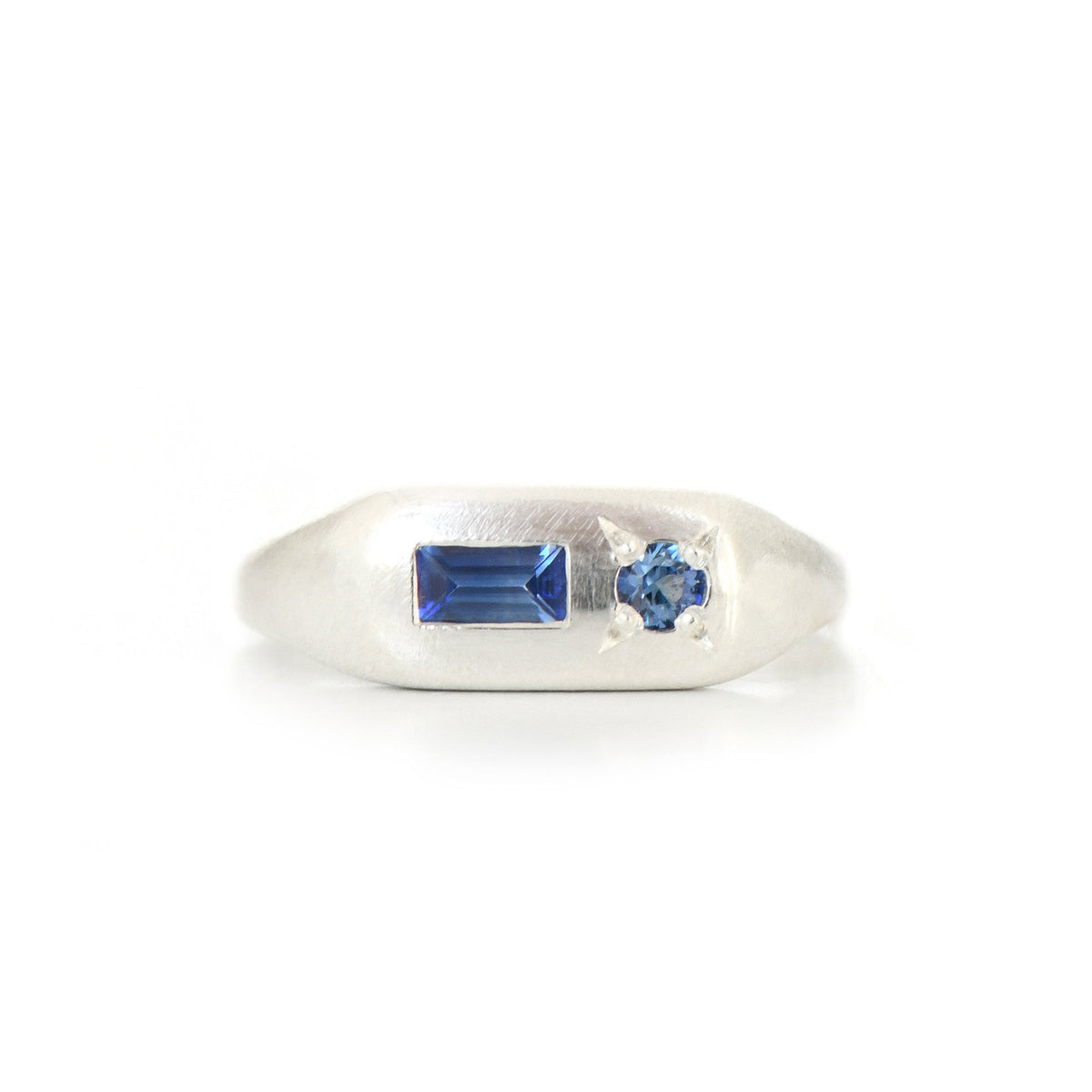 A silver ring featuring a rectangular blue gemstone and a small round blue gemstone on a white background.