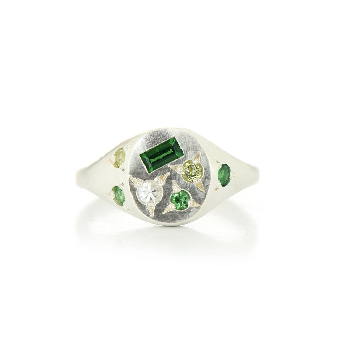 A silver signet ring with a mix of green and white gemstones on a white background
