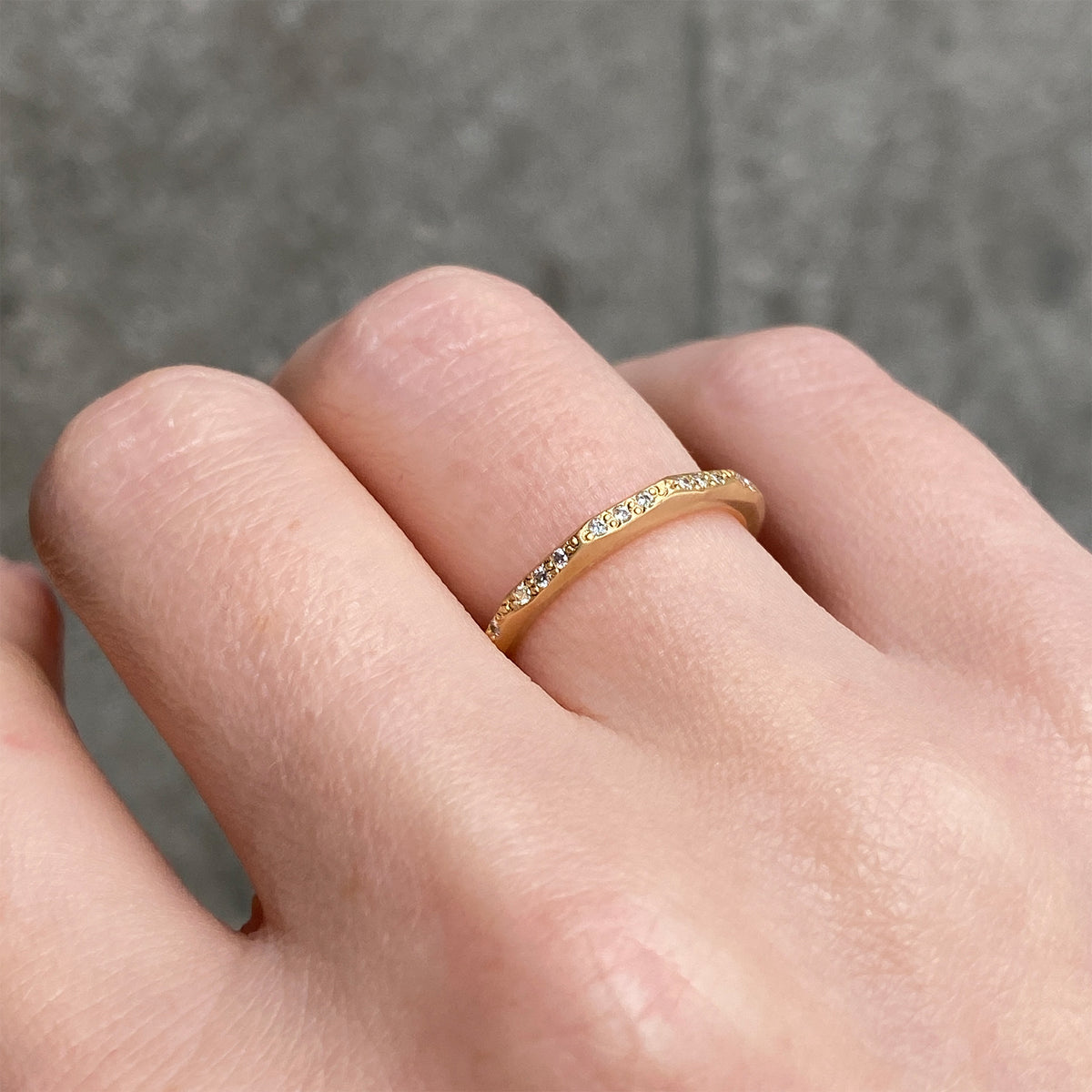 A close up of a hand wearing a delicate gold band ring with small diamonds set along the band