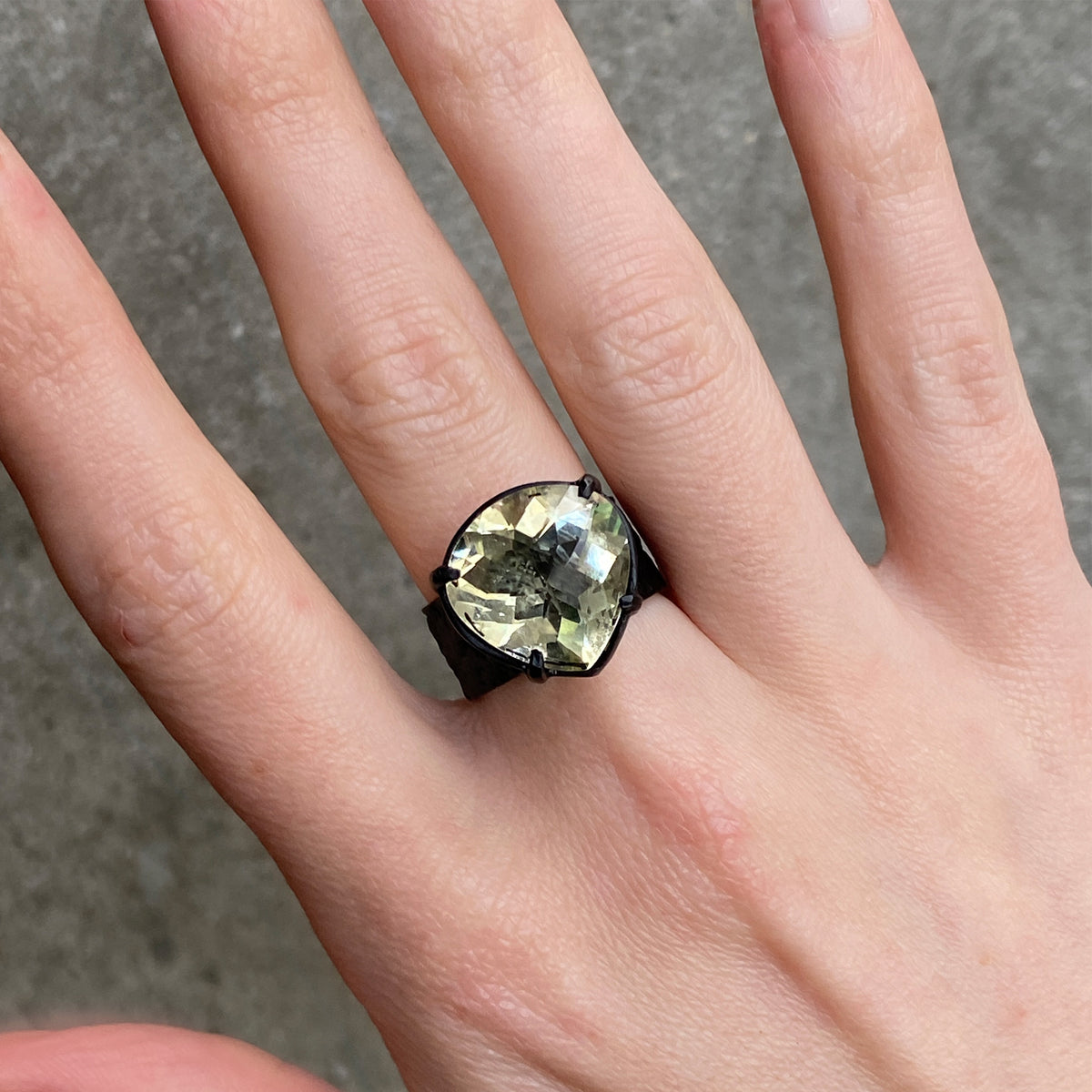 A close-up of a hand wearing a black ring with a large, faceted olive-green gemstone.