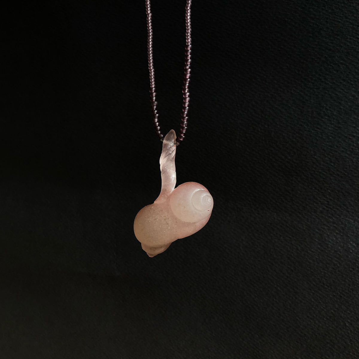 Pink glass pendant on fine beaded thread on a black background