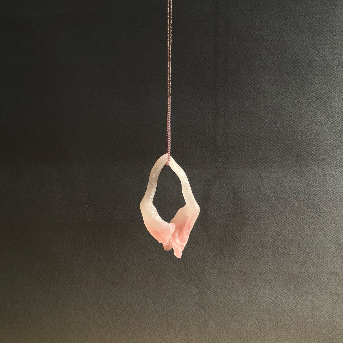 Pink glass pendant on fine beaded thread on a black background