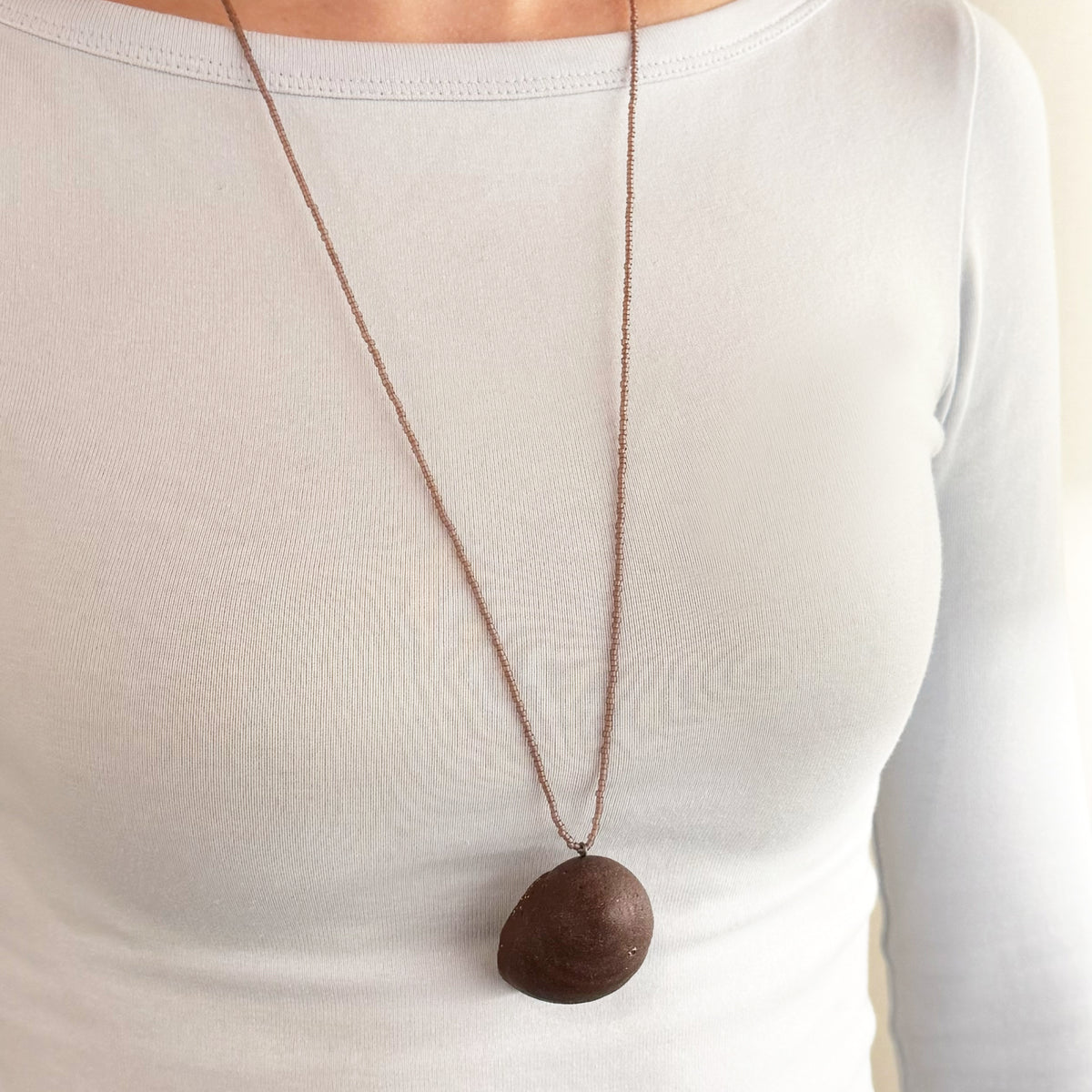 burgundy coloured pendant worn on body with a white background