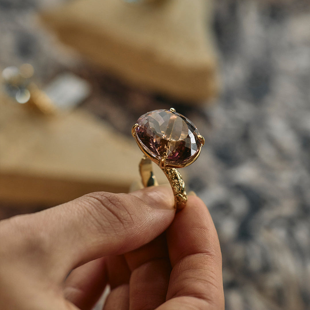 Gold ring with a large gemstone held by a hand against a blurred background