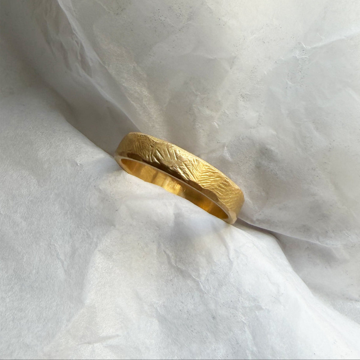 An organic textured yellow gold band ring resting on crumpled white paper.
