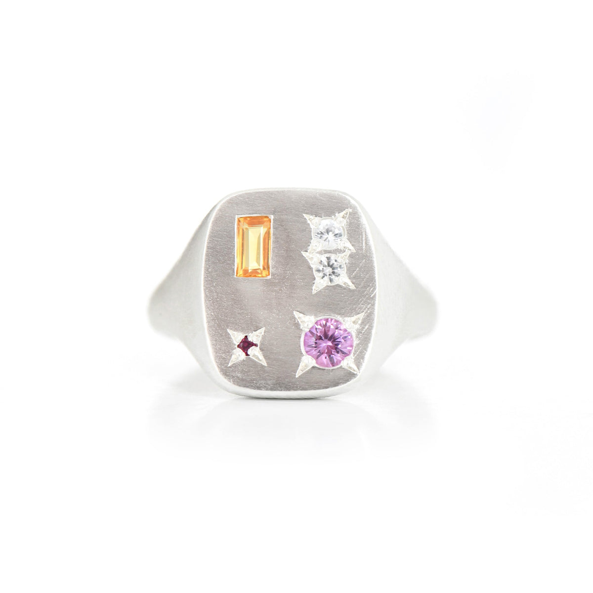 A silver signet ring featuring a rectangular face with multiple gemstones, including a rectangular orange stone, a round pink stone, and two clear stones, set against a plain white background.