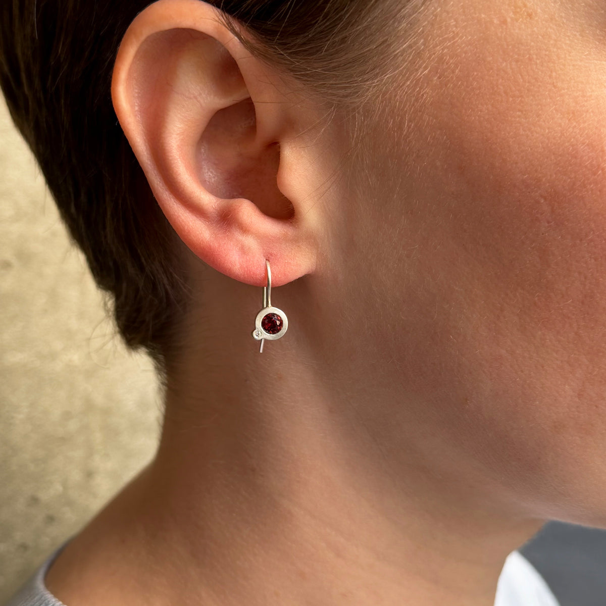 Round silver drop earrings with a garnet and a diamond worn on a model