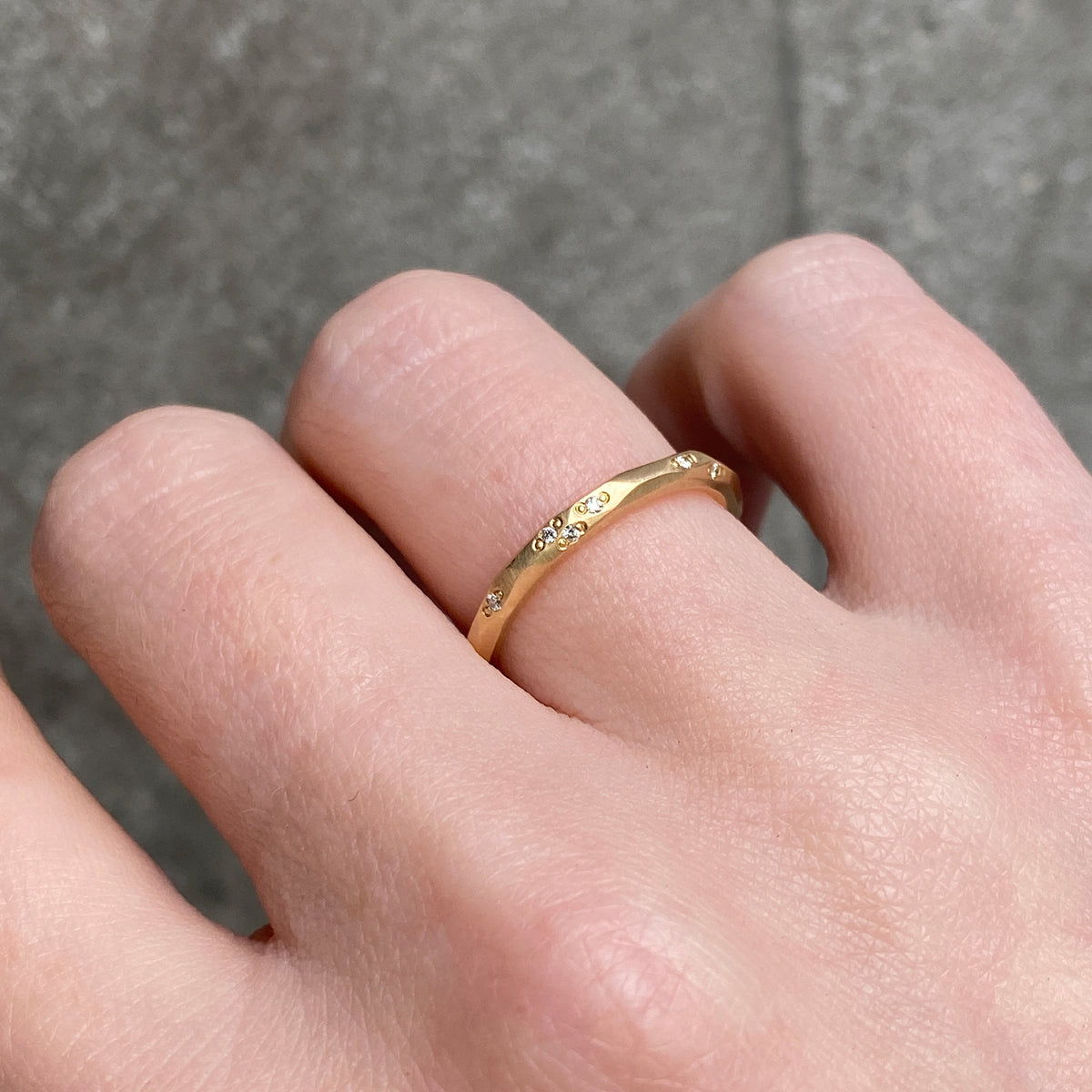 A close up of a hand wearing a delicate gold band ring with small diamonds set along the band