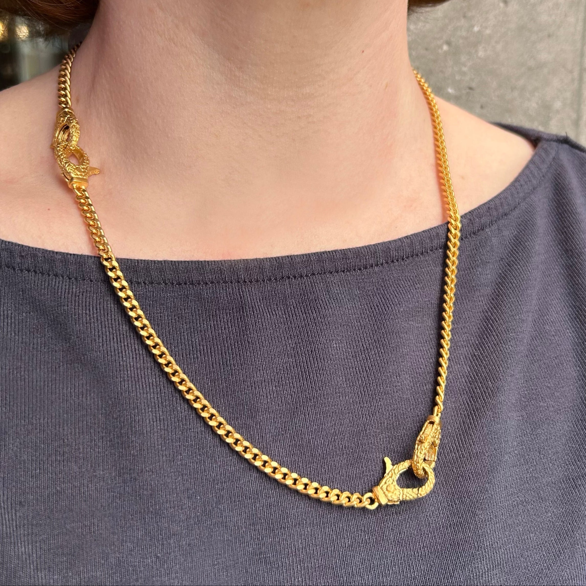 Gold chain necklace worn by a person against a neutral background