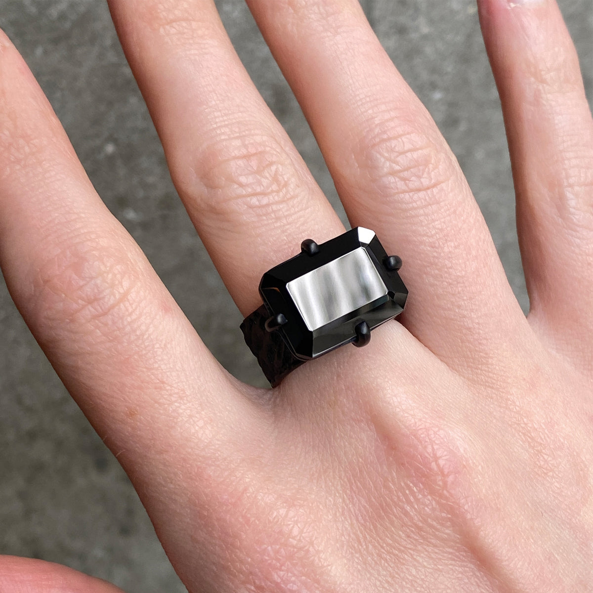 A close-up of a hand wearing a black ring with a rectangular faceted onyx stone in a claw setting