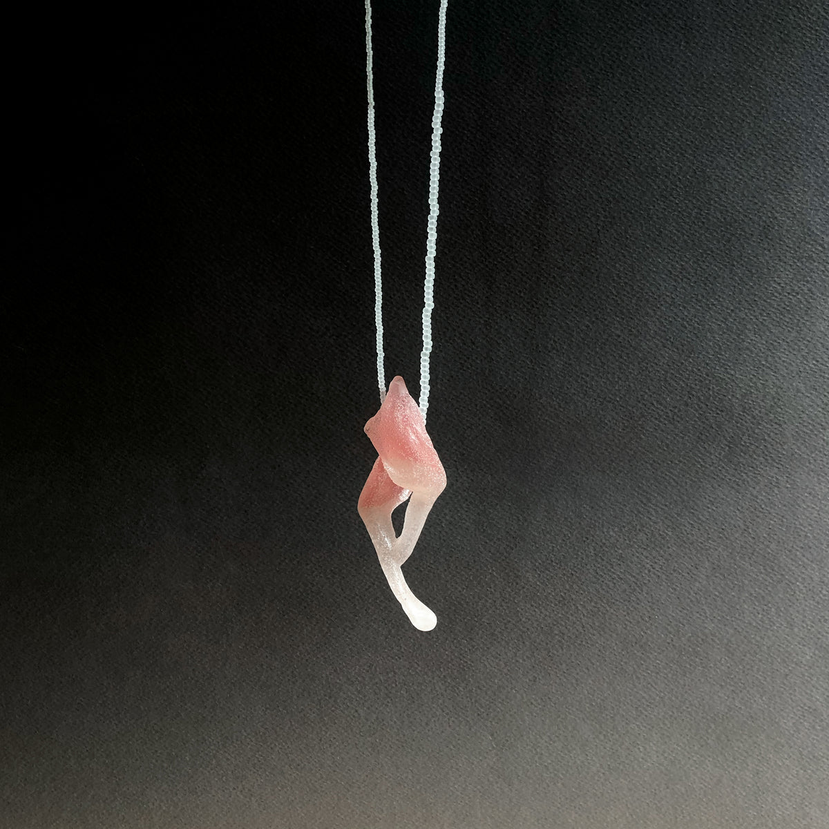 Pink glass pendant on fine beaded thread on a black background