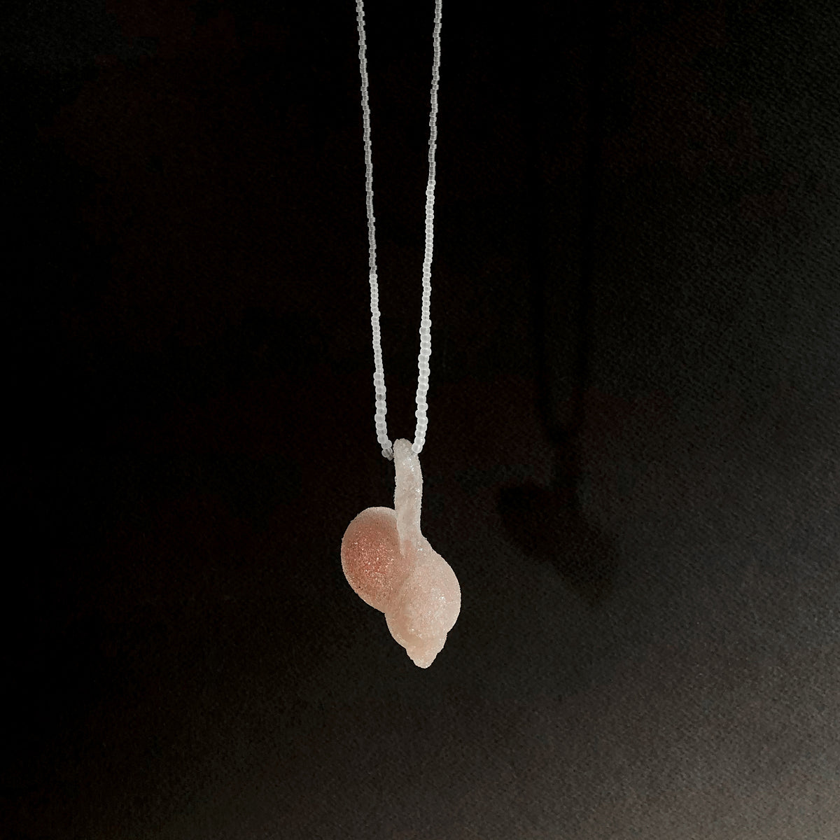 Pink glass pendant on fine beaded thread on a black background