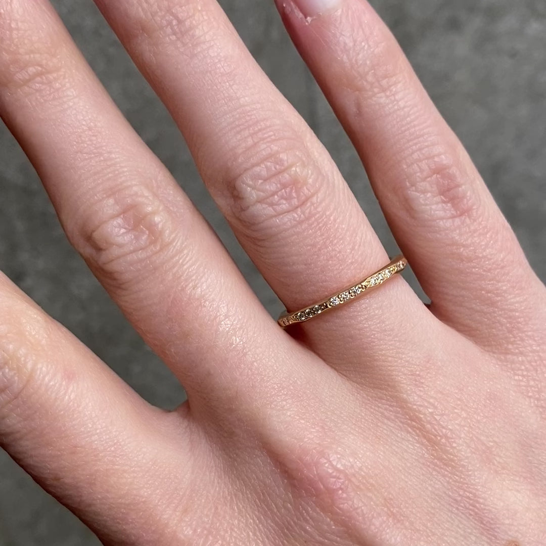 A close up of a hand wearing a delicate gold band ring with small diamonds set along the band