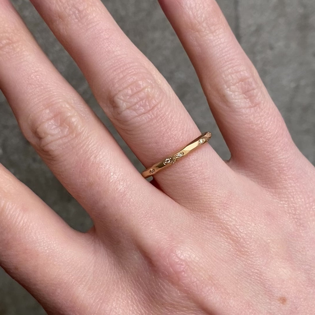 A close up of a hand wearing a delicate gold band ring with small diamonds set along the band