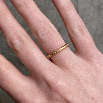 A close up of a hand wearing a delicate gold band ring with small diamonds set along the band